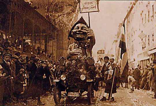 Mir frein uns - Ludwig Lipp am Steuer seines Wagens Rosenmontagszug 1927, neben dem Traktor steht ein Fahnenträger, rechts und links säumt das Publikum den Zugweg